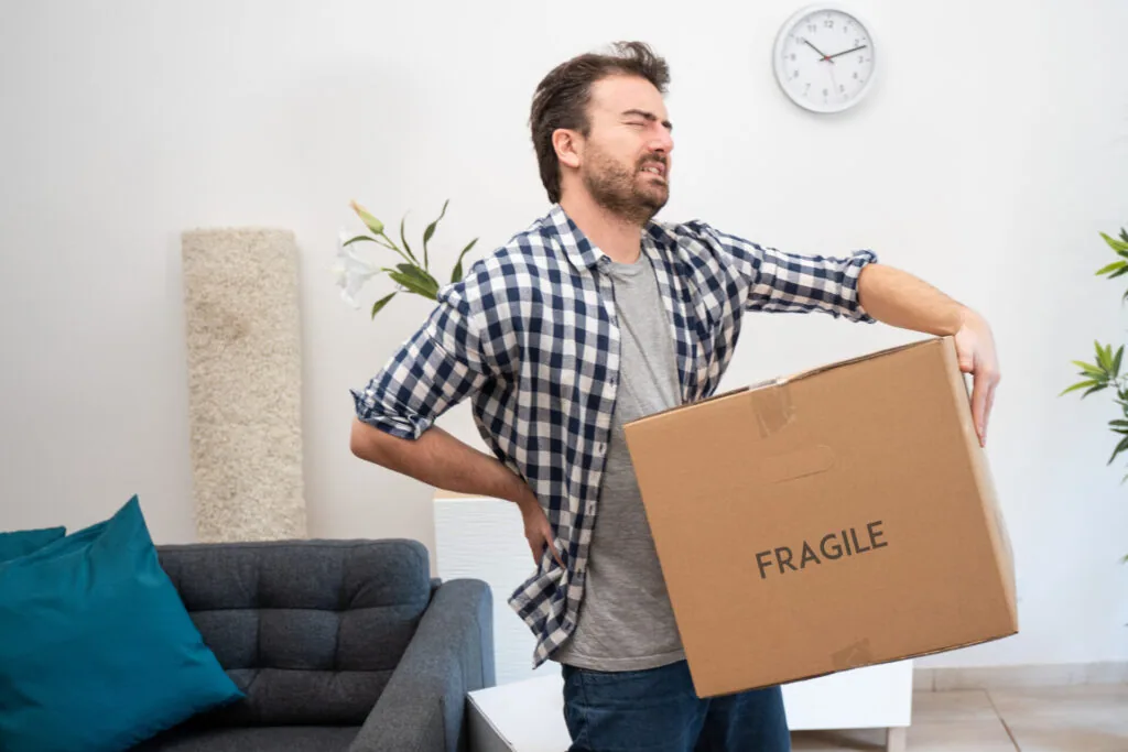 Man in checkered shirt holding cardboard box labeled FRAGILE in living room with furniture