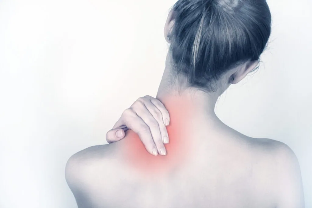 Woman with dark hair in a bun touching her upper back and shoulder with a red highlighted pain area