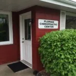 Red building entrance with white door and Florian Chiropractic Center sign, green shrub beside doorway