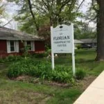 White business sign for Florian Chiropractic Center in front of red brick building with large tree
