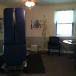 Chiropractic office interior with blue spinal decompression equipment, skeleton model, ceiling fan with lights, and window
