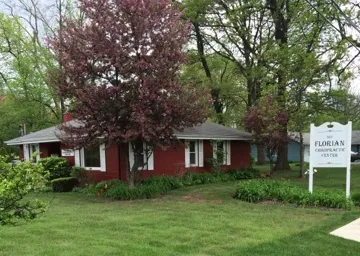 Red brick single-story chiropractic office building with white trim, large trees, and landscaping in front lawn