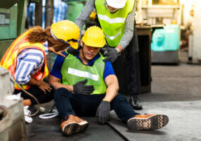 First Aid. Engineering supervisor talking on walkie talkie communication while his coworker lying unconscious at industrial factory. Professional engineering teamwork concept.